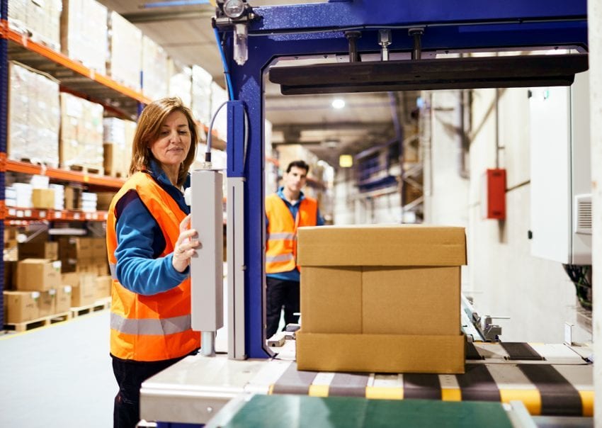 Two warehouse workers in hi-vis vests beside a case on a conveyor